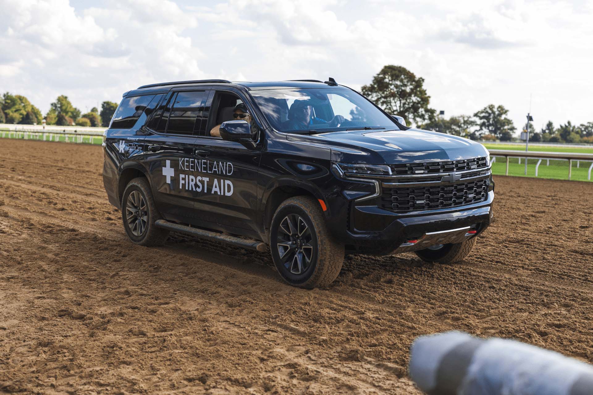 A picture of the Keenfields First Aid car on the dirt track. It is a large black Chevy SUV.